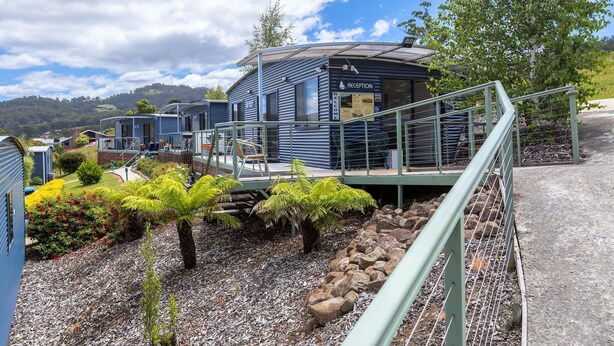 A reception area with a sign, a covered walkway, and a view of the surrounding landscape. - Port Huon Cottages (Port Huon)