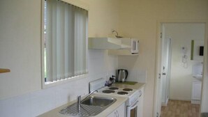 A compact kitchen with a sink, stove, and microwave. - Port Huon Cottages (Port Huon)