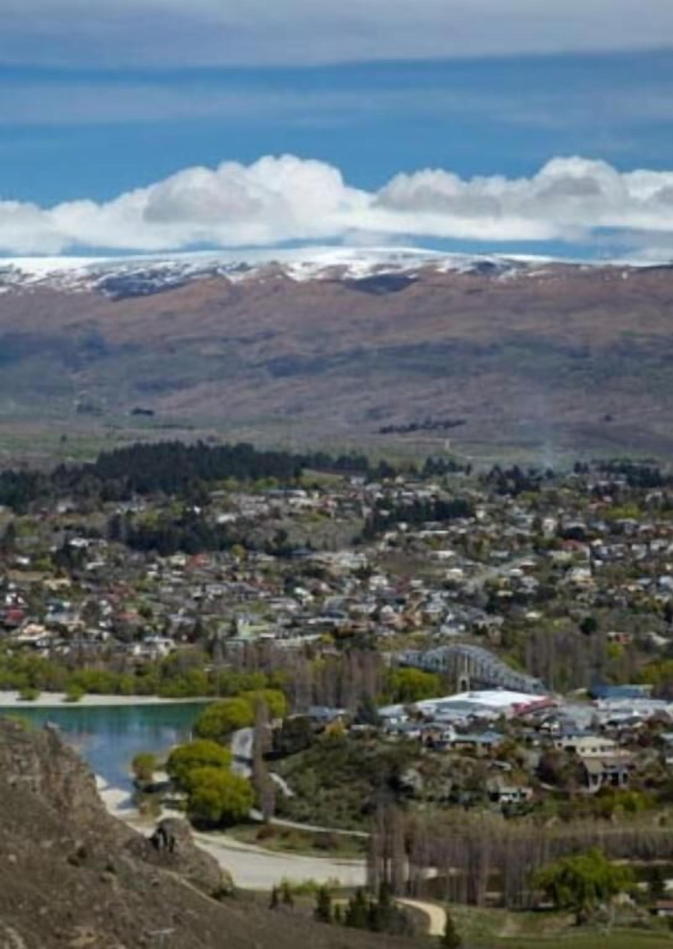 A town with a mix of residential and commercial buildings, a body of water, and a mountainous backdrop.
