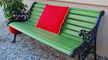 Un banco verde con cojín rojo, reposabrazos metálicos y una planta a su lado.