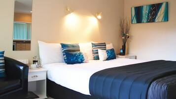 A hotel room with a bed, bedside tables, a nightstand, a lamp, a vase with branches, and a painting on the wall.