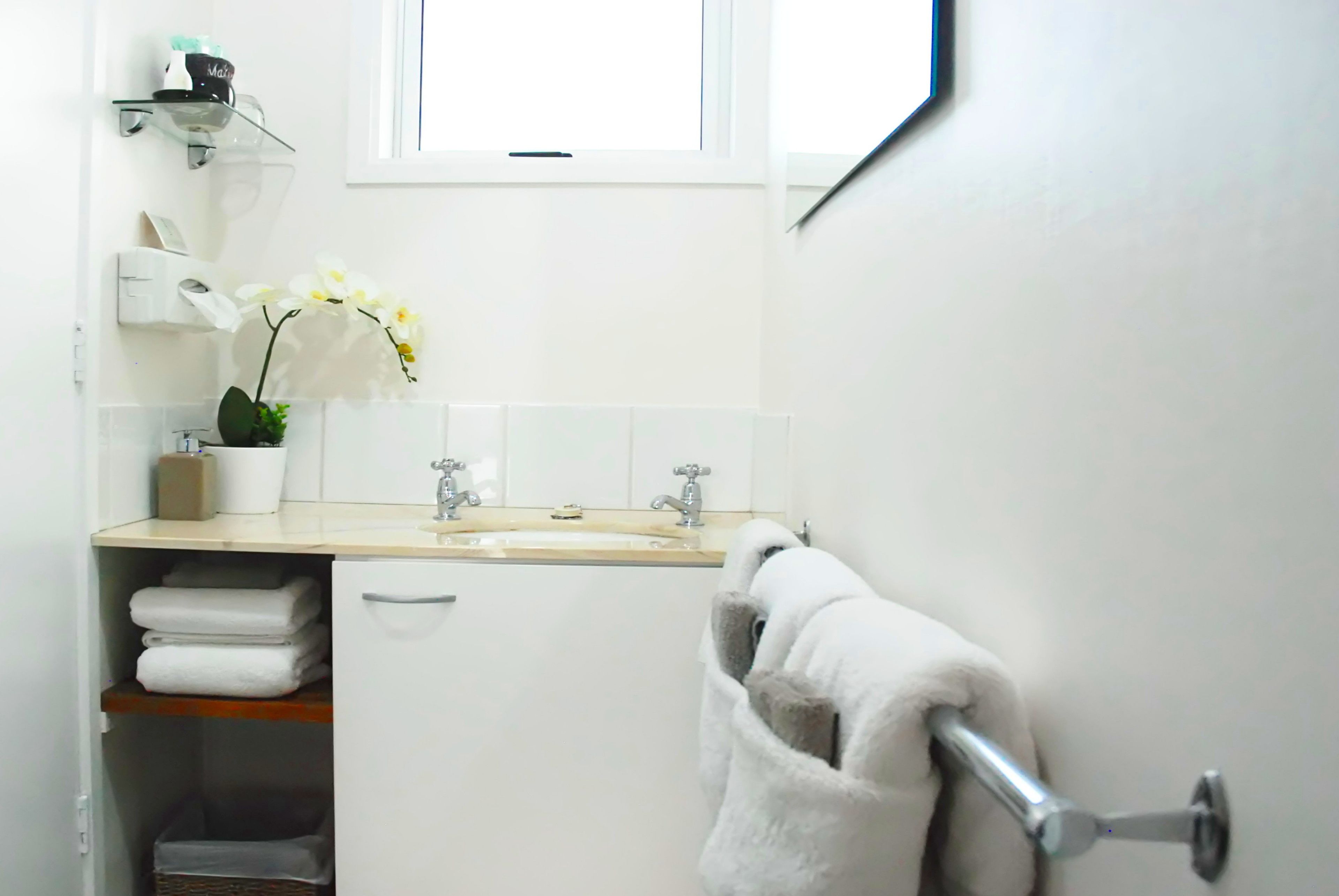 A bathroom with a sink, two faucets, a towel rack, and a window.