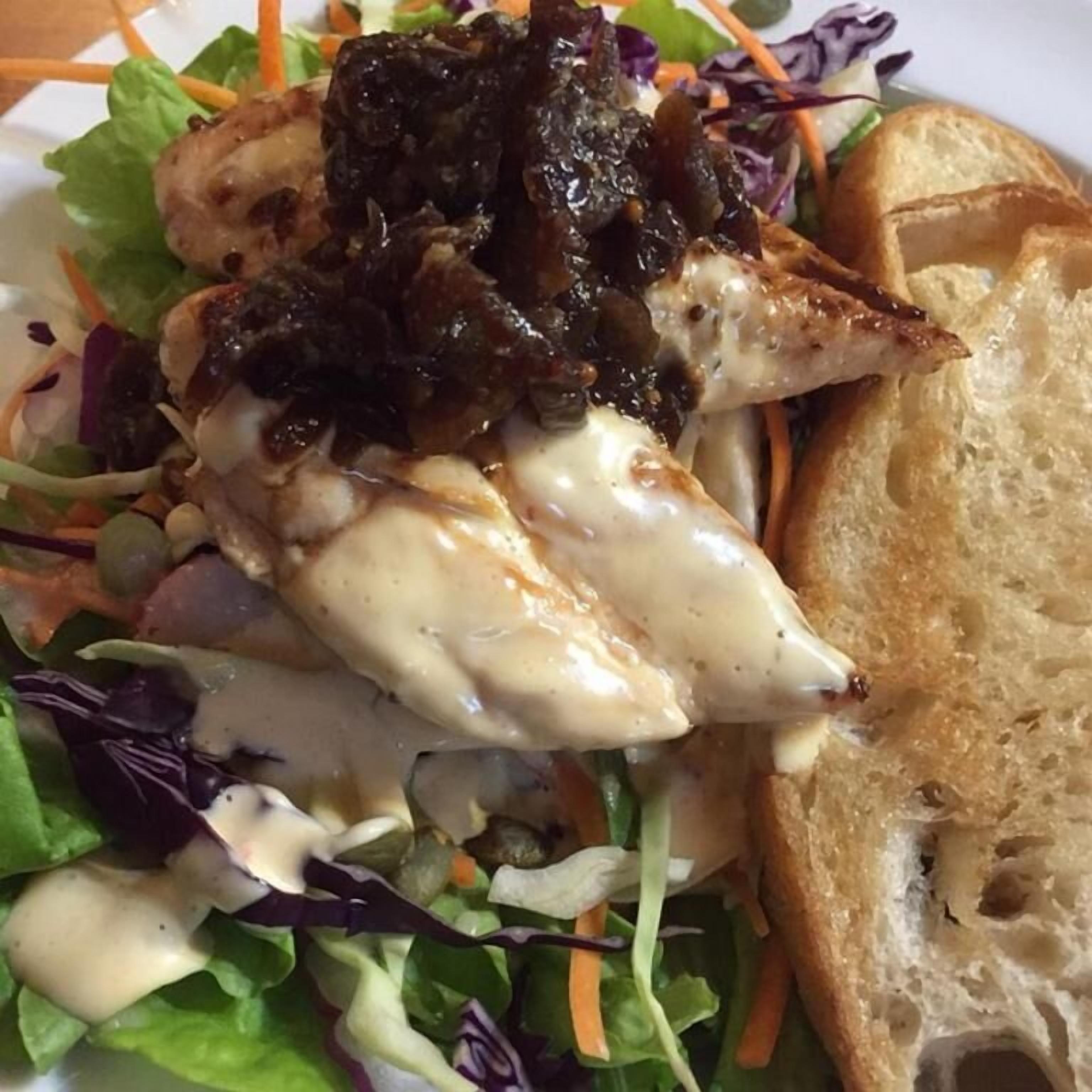 Een bord met gegrilde kip, een salade en een stuk brood.