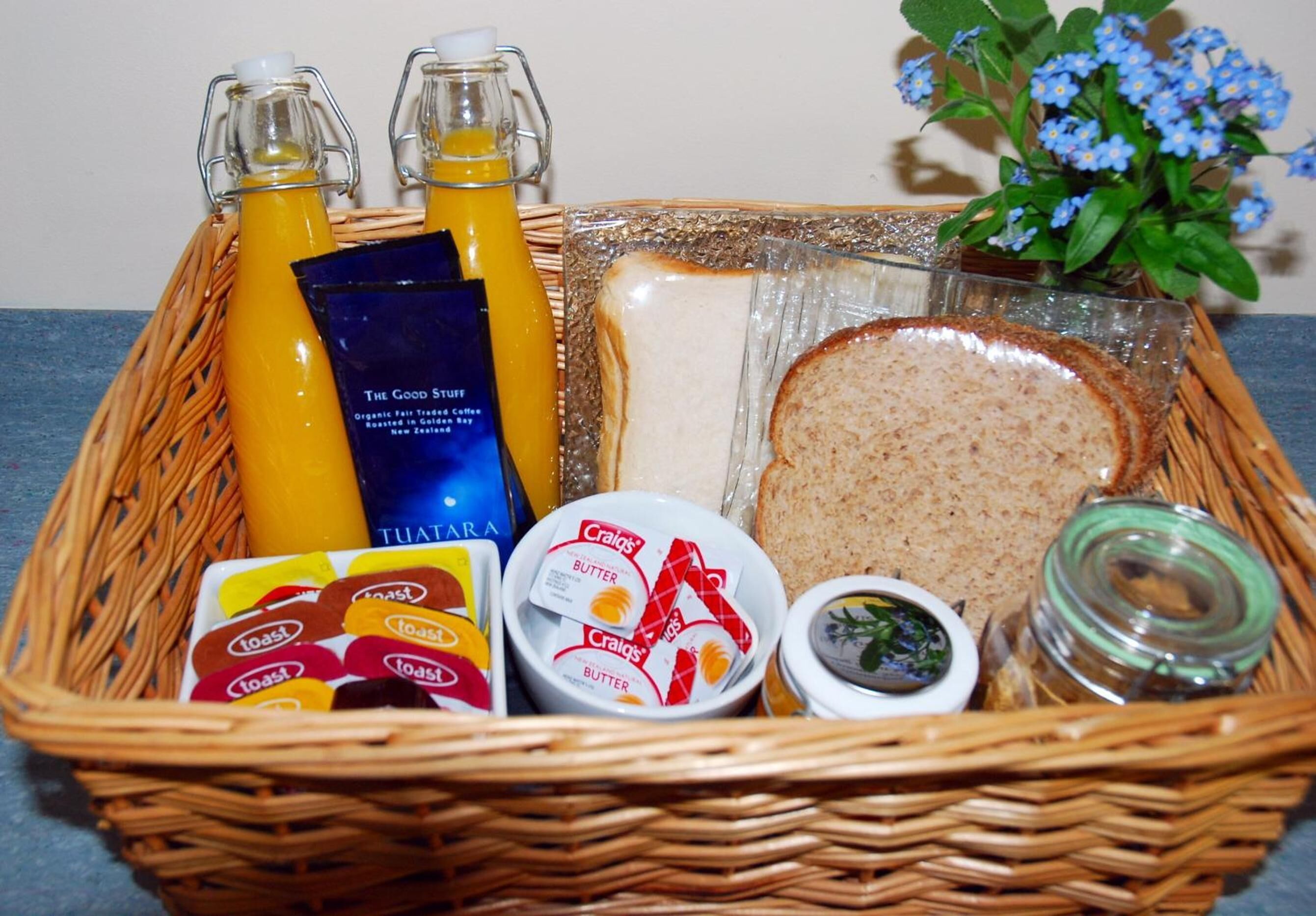 A wicker basket containing breakfast items including toast, butter, juice, and a jar of jam.
