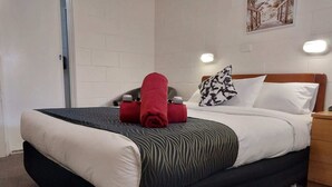 Una cama bien tendida con un edredón a rayas blancas y negras, una toalla roja y una almohada estampada.