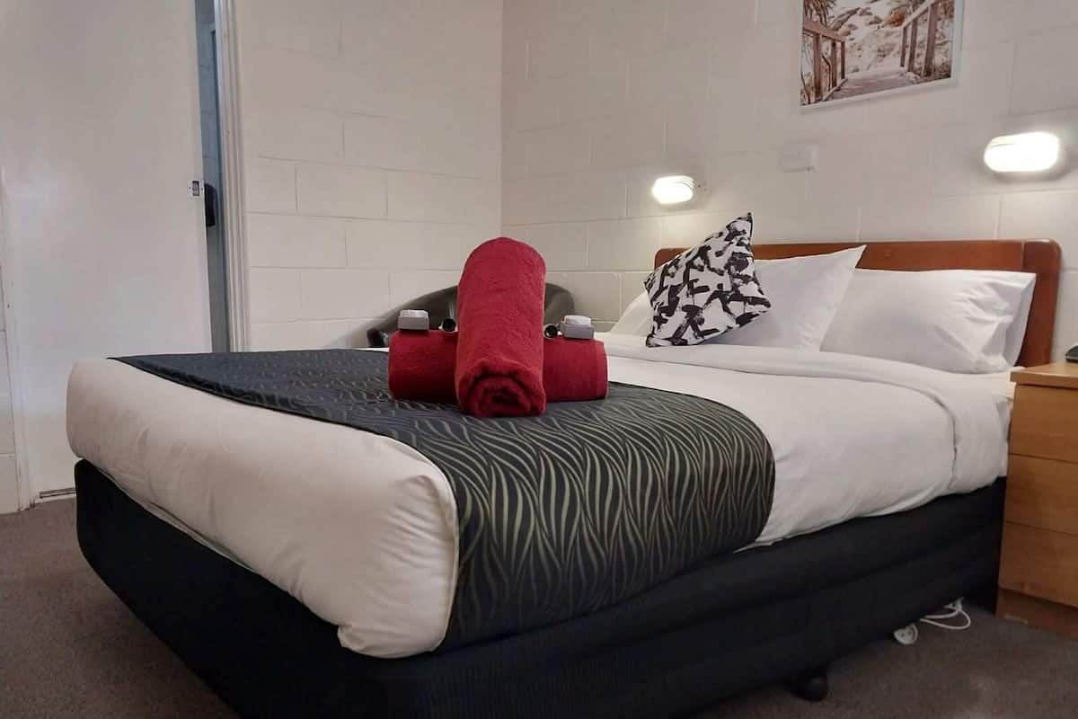 A neatly made bed with a white and black striped bedspread, a red towel, and a patterned pillow.