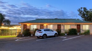 Un motel con techo verde, habitaciones numeradas y un estacionamiento.