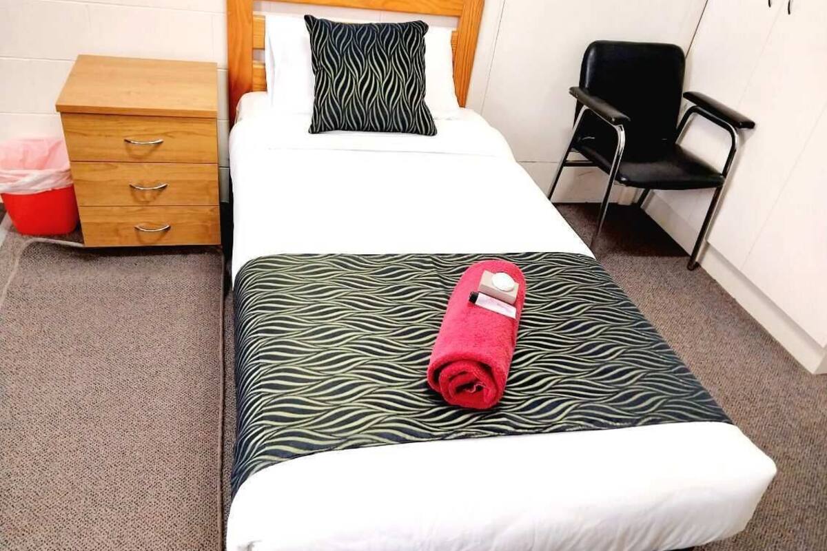 A single bed with a zebra-patterned bedspread and a red towel, a wooden nightstand with drawers, a black chair, and a white wall.