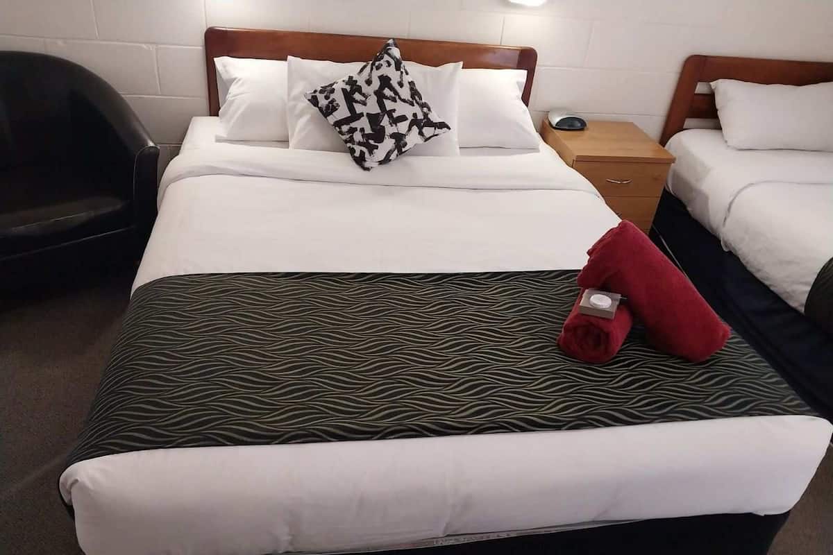 A hotel room with a large bed, two bedside tables, a chair, and a nightstand with a lamp.