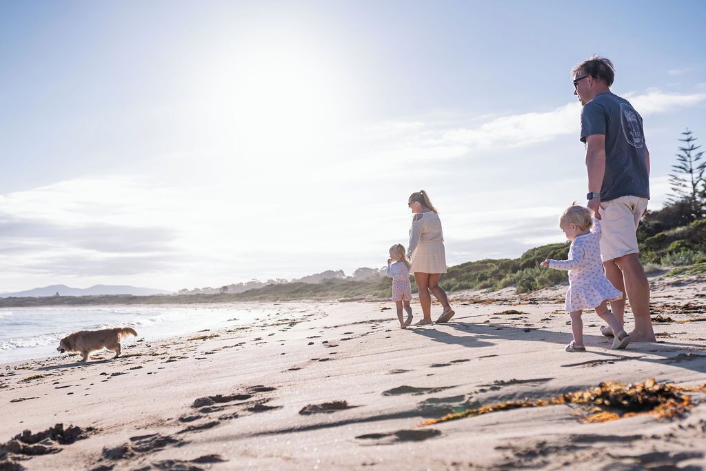 Una familia caminando sobre una playa arenosa con un perro, bajo un cielo despejado.