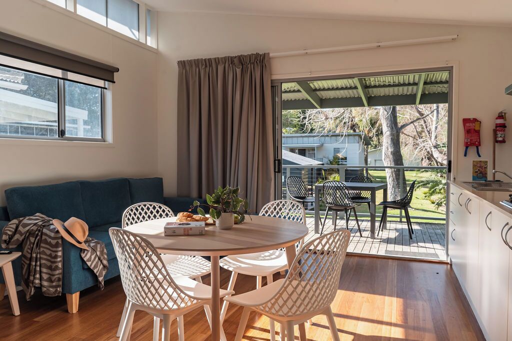 Una sala de estar moderna con sofá, mesa de comedor y sillas. Hay un balcón con mobiliario exterior y vistas al exterior.