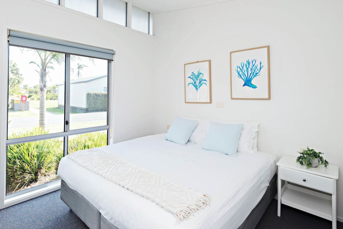Une chambre moderne avec un grand lit, une table de chevet et une fenêtre donnant sur un paysage verdoyant.