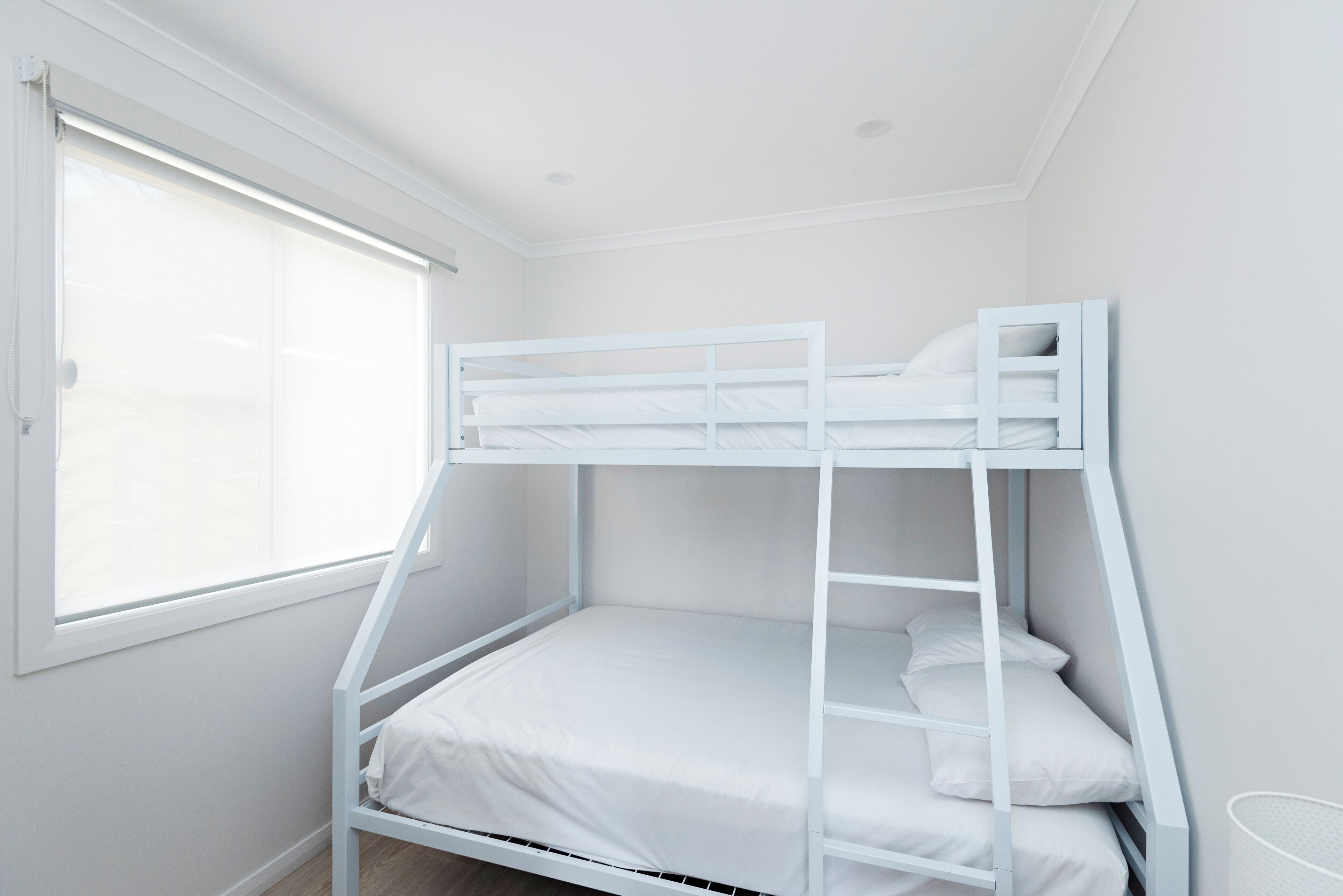 A bunk bed with a ladder, white bedding, and a window with blinds.