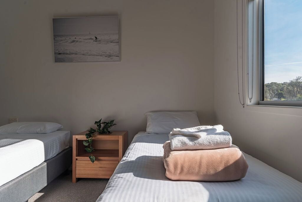 Une chambre à coucher avec un lit, une table de chevet ornée d’une plante et une fenêtre donnant sur l’extérieur.