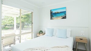 Un dormitorio con una cama grande, una ventana con vista a vegetación, una mesita de noche y un cuadro colgado en la pared.