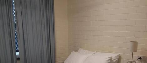 Habitación de hotel con dos camas, una cortina azul, una pared de ladrillo blanco y un ventilador de techo.