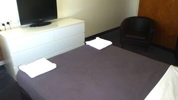 A hotel room with a bed, a TV on a dresser, a chair, and a wooden door.