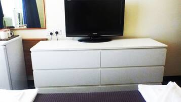 A hotel room with a flat-screen TV on a white dresser, a small refrigerator, and a bed with a dark headboard.