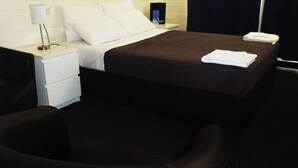Ein Hotelzimmer mit Bett, Nachttisch, Lampe, Stuhl und gefaltetem Handtuch.