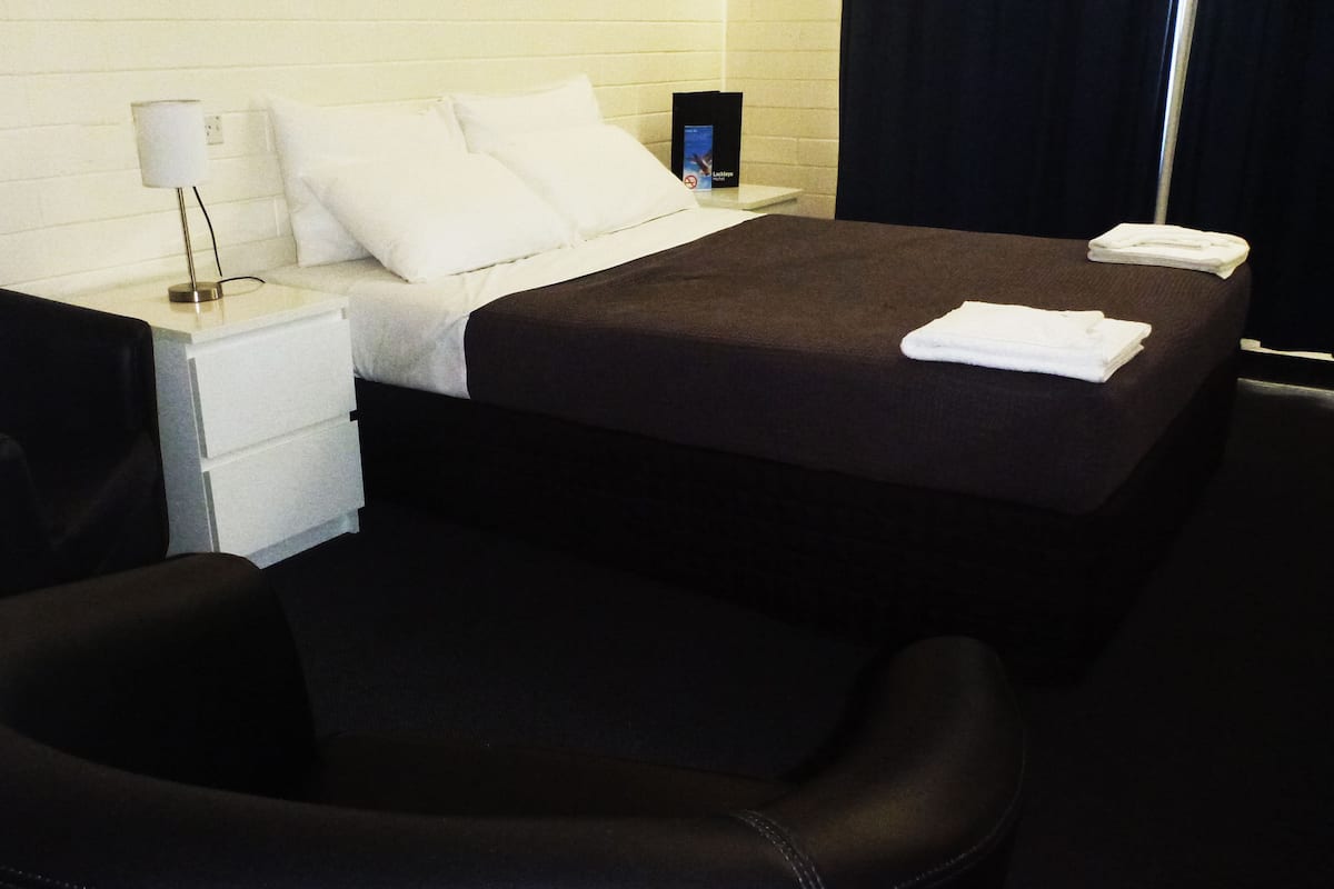 A hotel room with a bed, a nightstand, a lamp, a chair, and a folded towel.