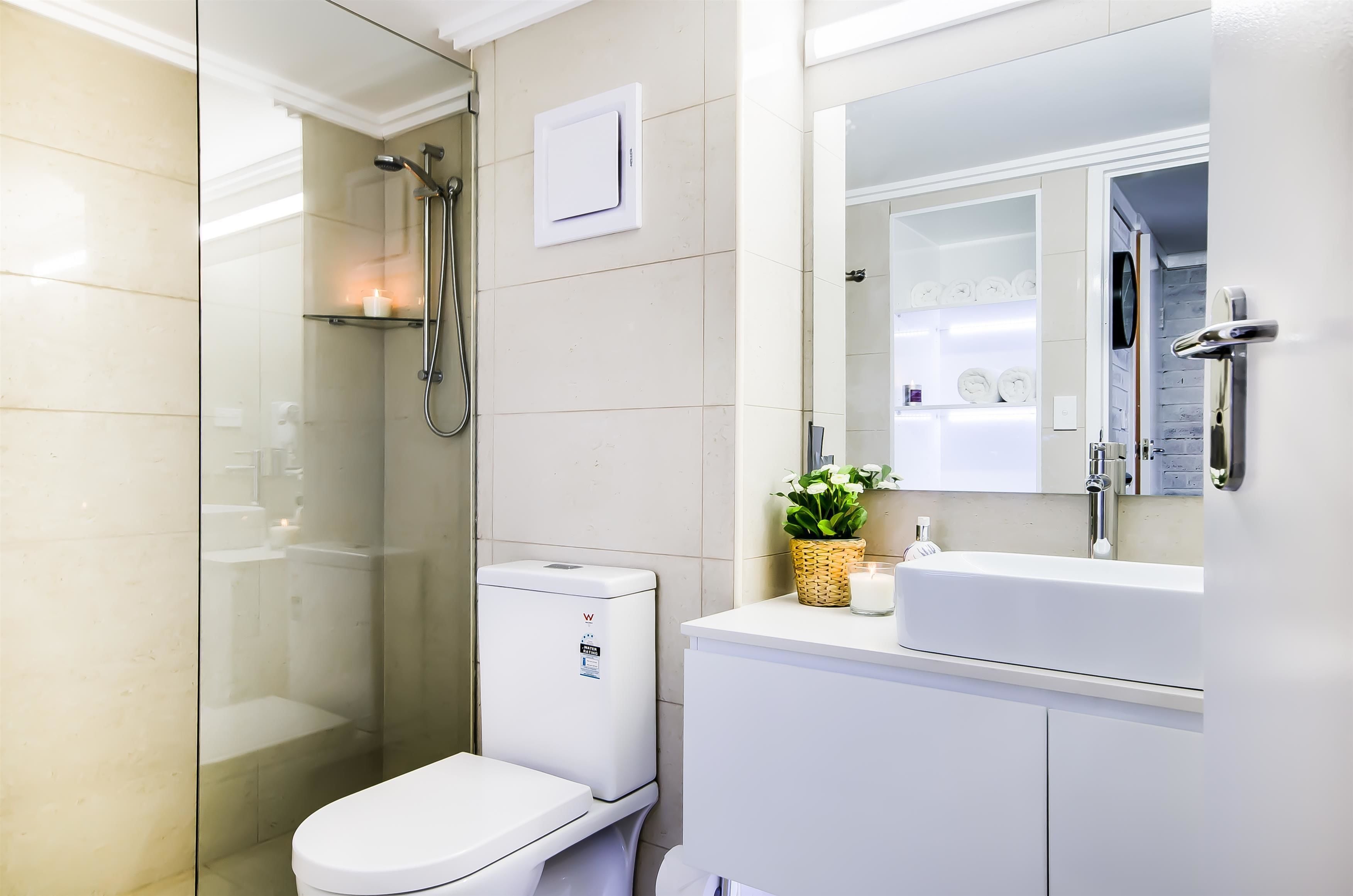 A modern bathroom with a glass-enclosed shower, a toilet, a sink with a mirror, and a small shelf with toiletries.
