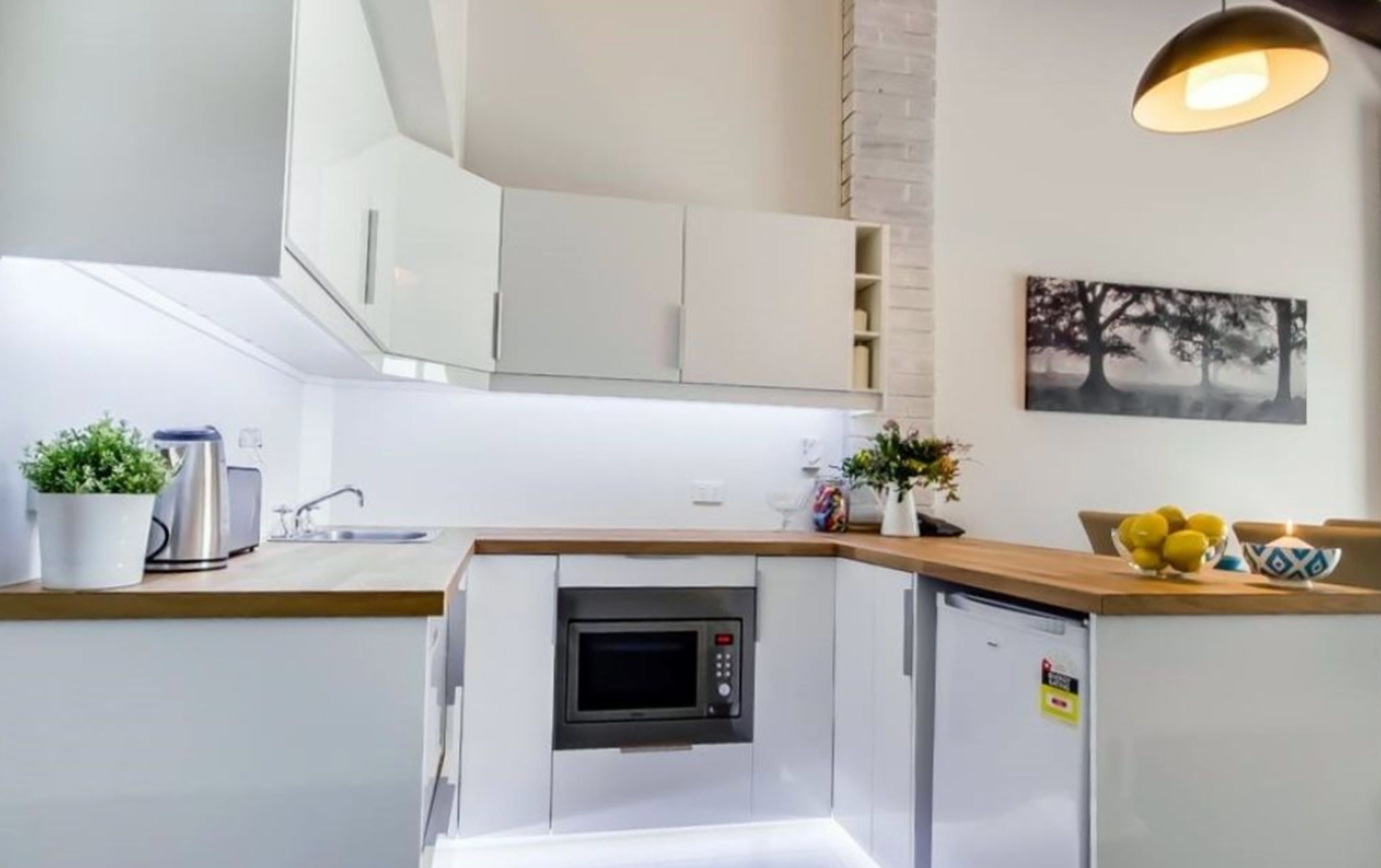 A compact kitchen with white cabinets, a built-in microwave, a sink, and a small refrigerator.