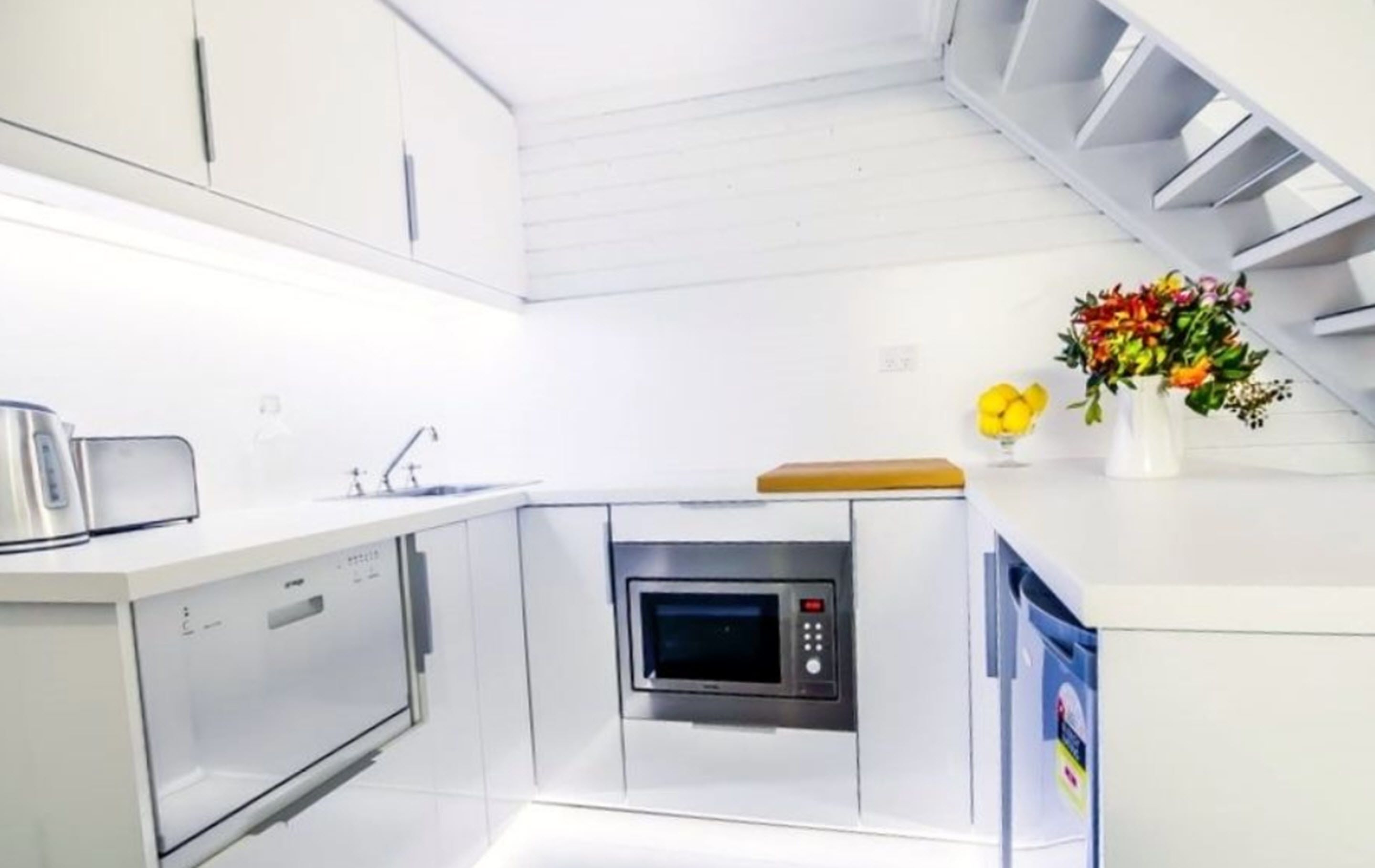 Une cuisine compacte dotée d’un four à micro-ondes encastré, d’un petit évier et d’un plan de travail en bois.