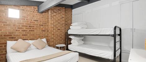 Ein Schlafzimmer mit Backsteinwand, Etagenbett, einem Einzelbett mit Kissen und einem weißen Kleiderschrank.