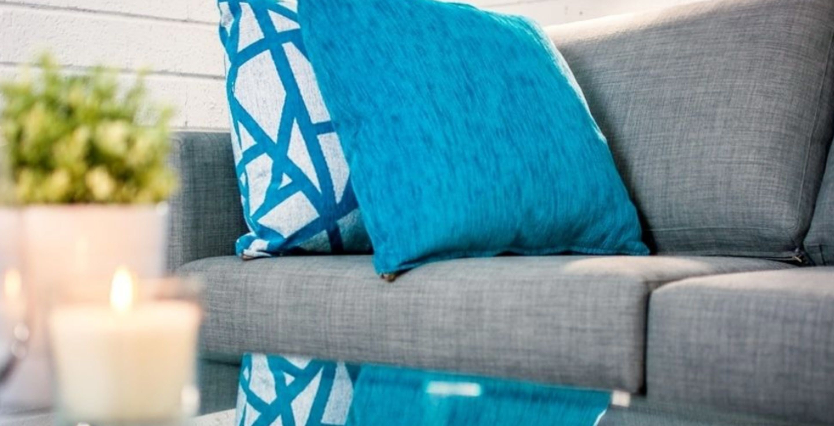 A grey sofa with a blue geometric-patterned pillow and a white candle in the background.