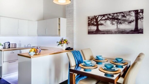A modern kitchen with white cabinets, a wooden island, and a dining area with a table set for four.
