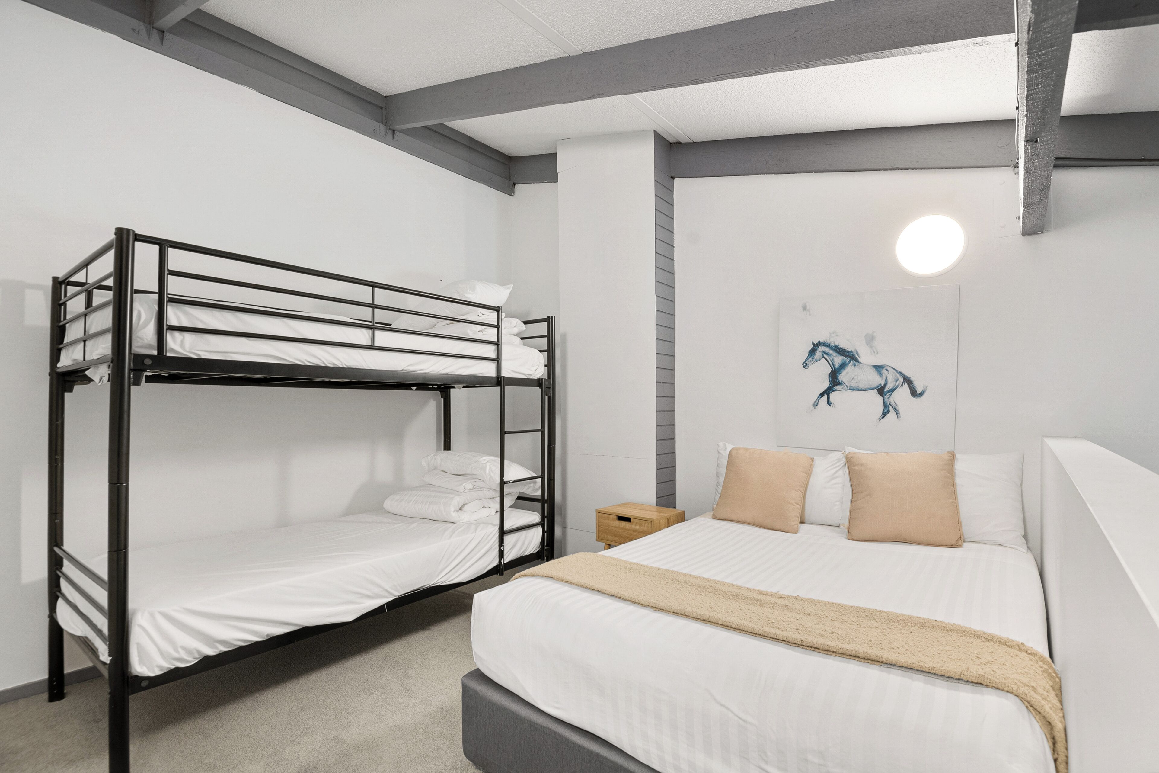 Un lit superposé avec une literie blanche et un lit simple avec une literie beige.