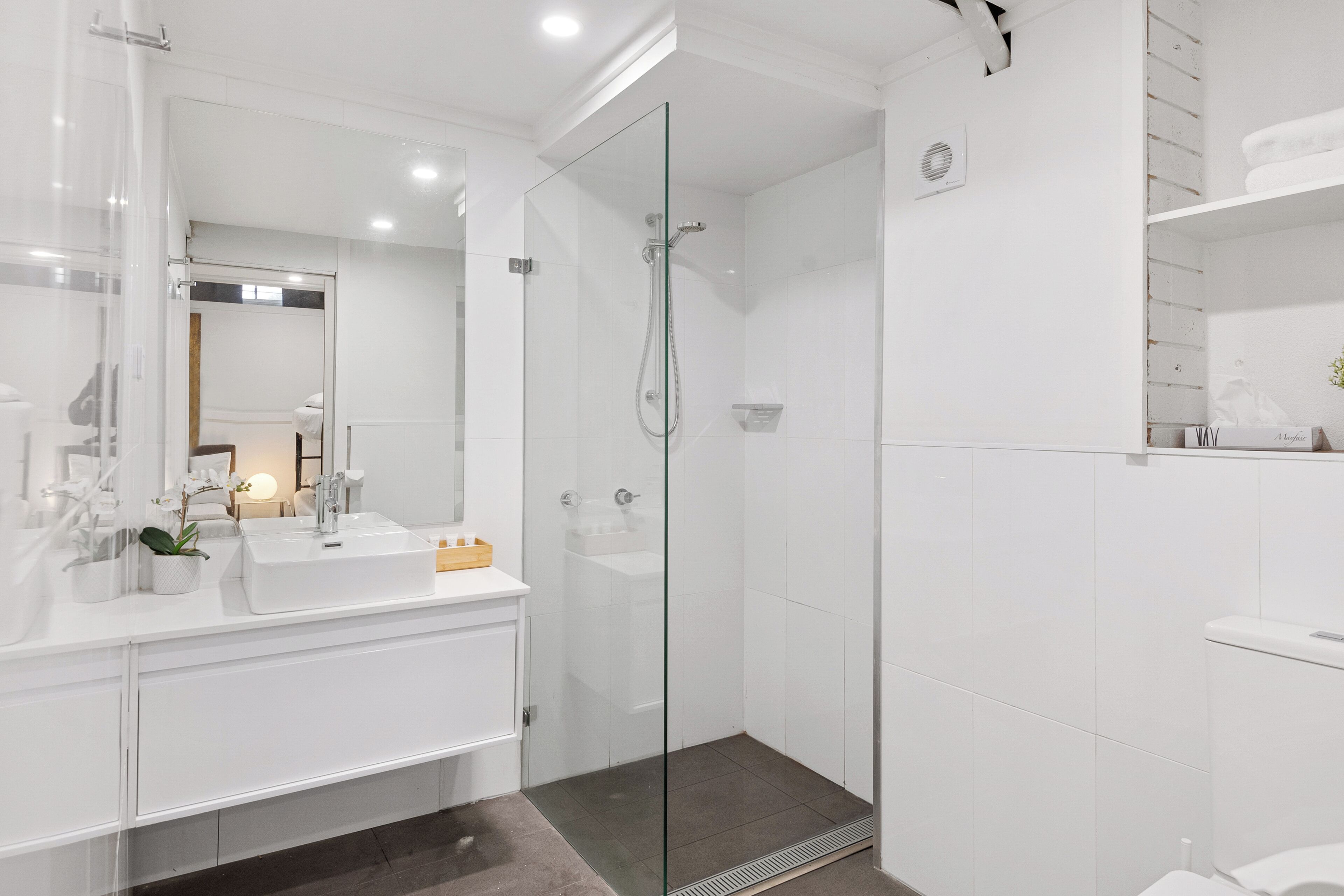 A modern bathroom with a glass-enclosed shower, white fixtures, and a large mirror.