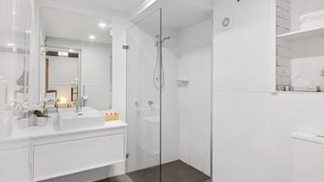 A modern bathroom with a glass-enclosed shower, white fixtures, and a large mirror.