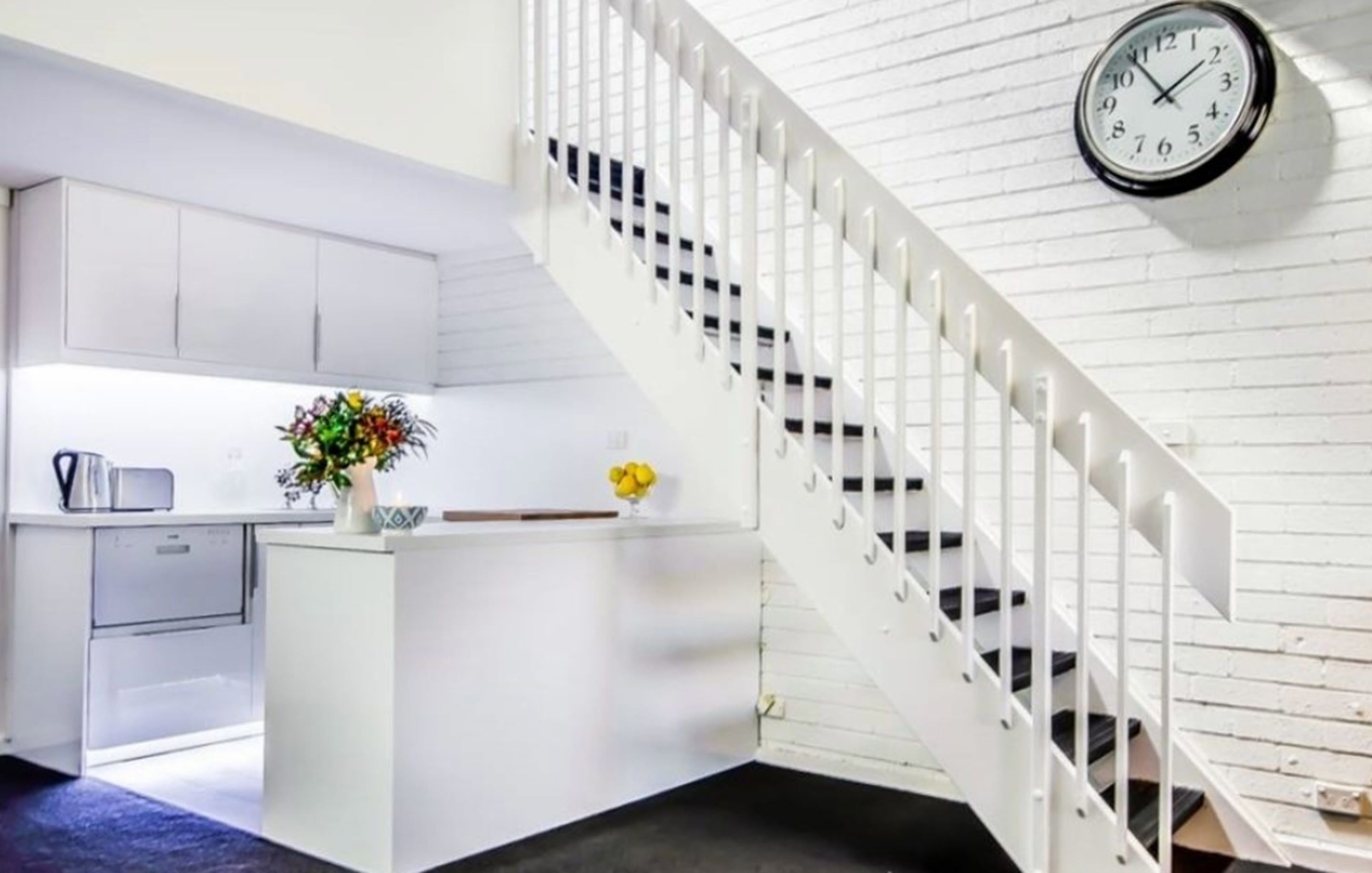 Une cuisine moderne avec des meubles blancs, un îlot central intégré et un escalier blanc.
