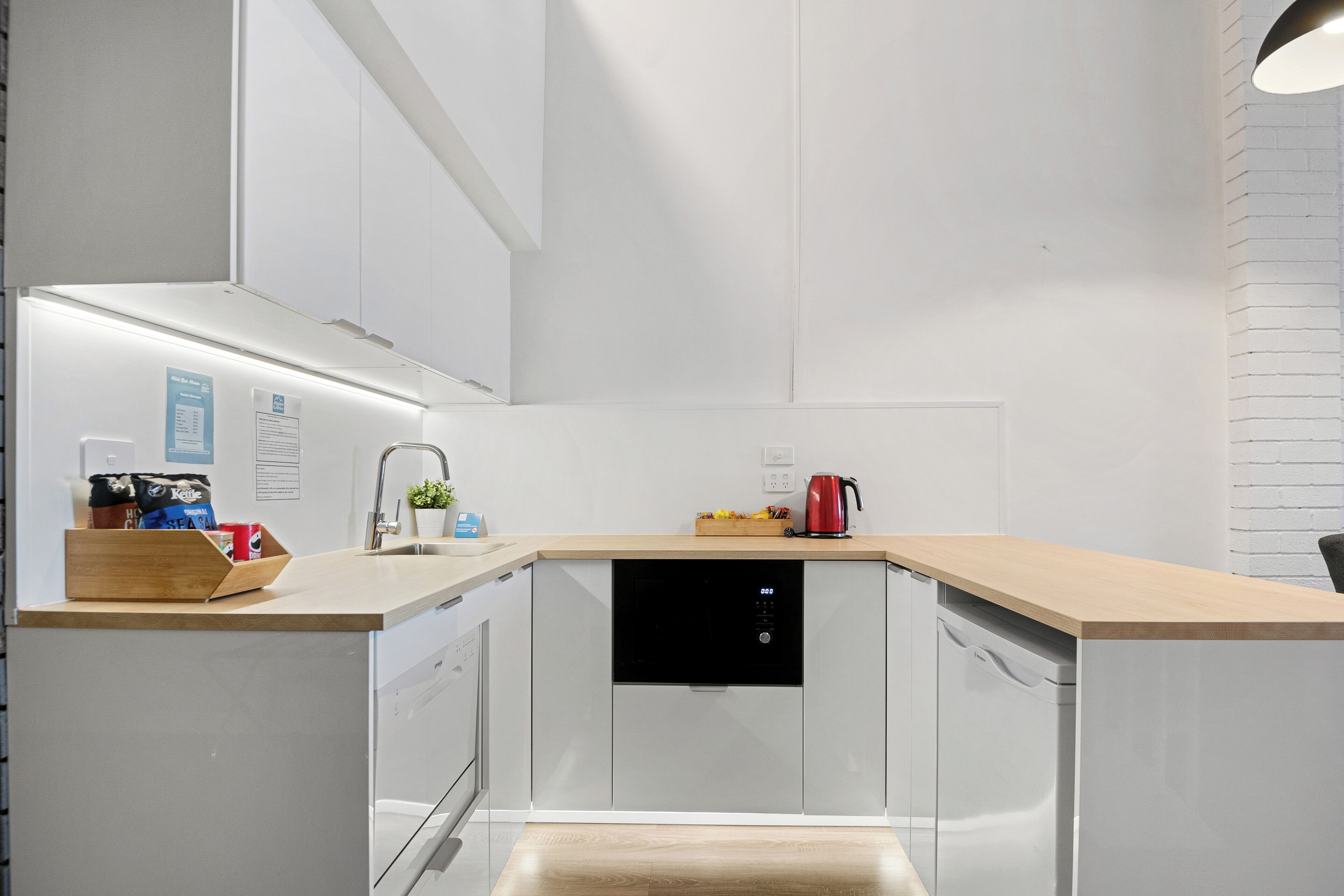 Eine moderne Küche mit weißen Schränken, einer Holz Arbeitsplatte, einem integrierten Geschirrspüler und einer Kaffeemaschine.