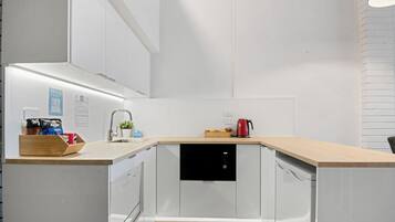Une cuisine moderne avec des meubles blancs, un plan de travail en bois, un lave-vaisselle encastré et une machine à café.