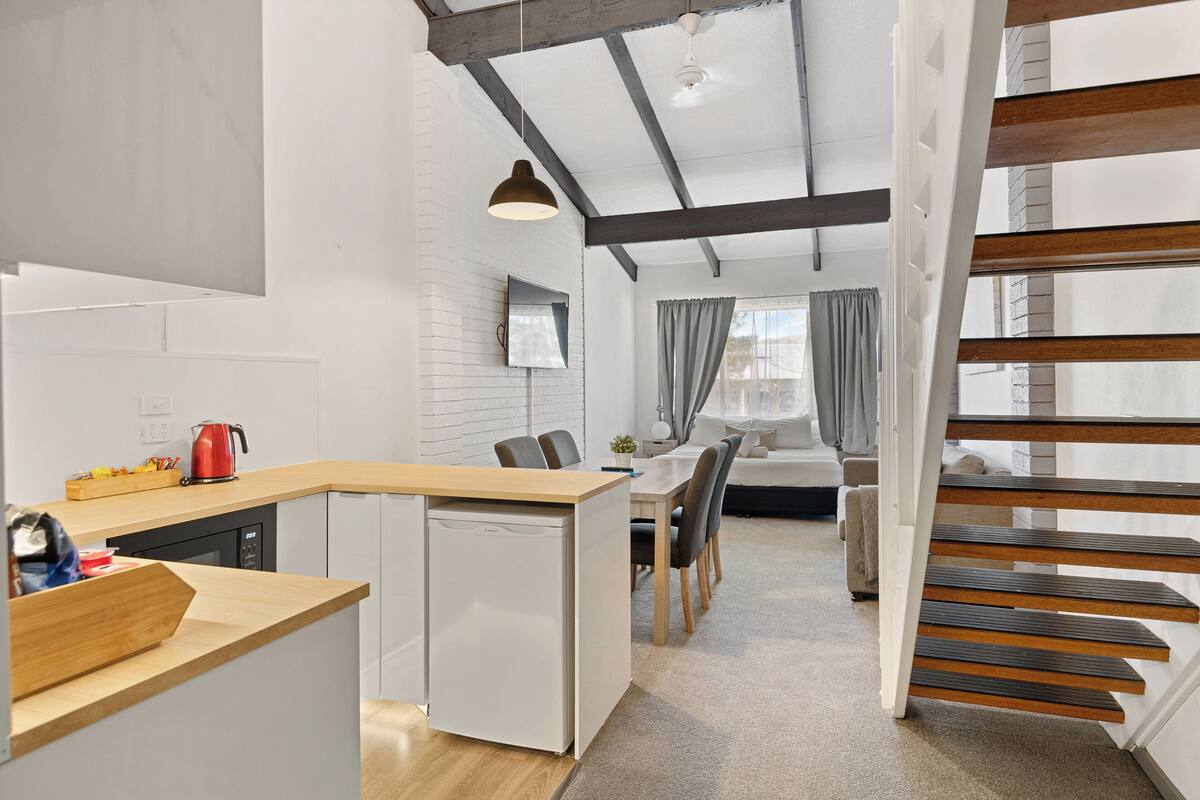 A modern kitchen with a built-in dishwasher, a wooden counter, and a red kettle.