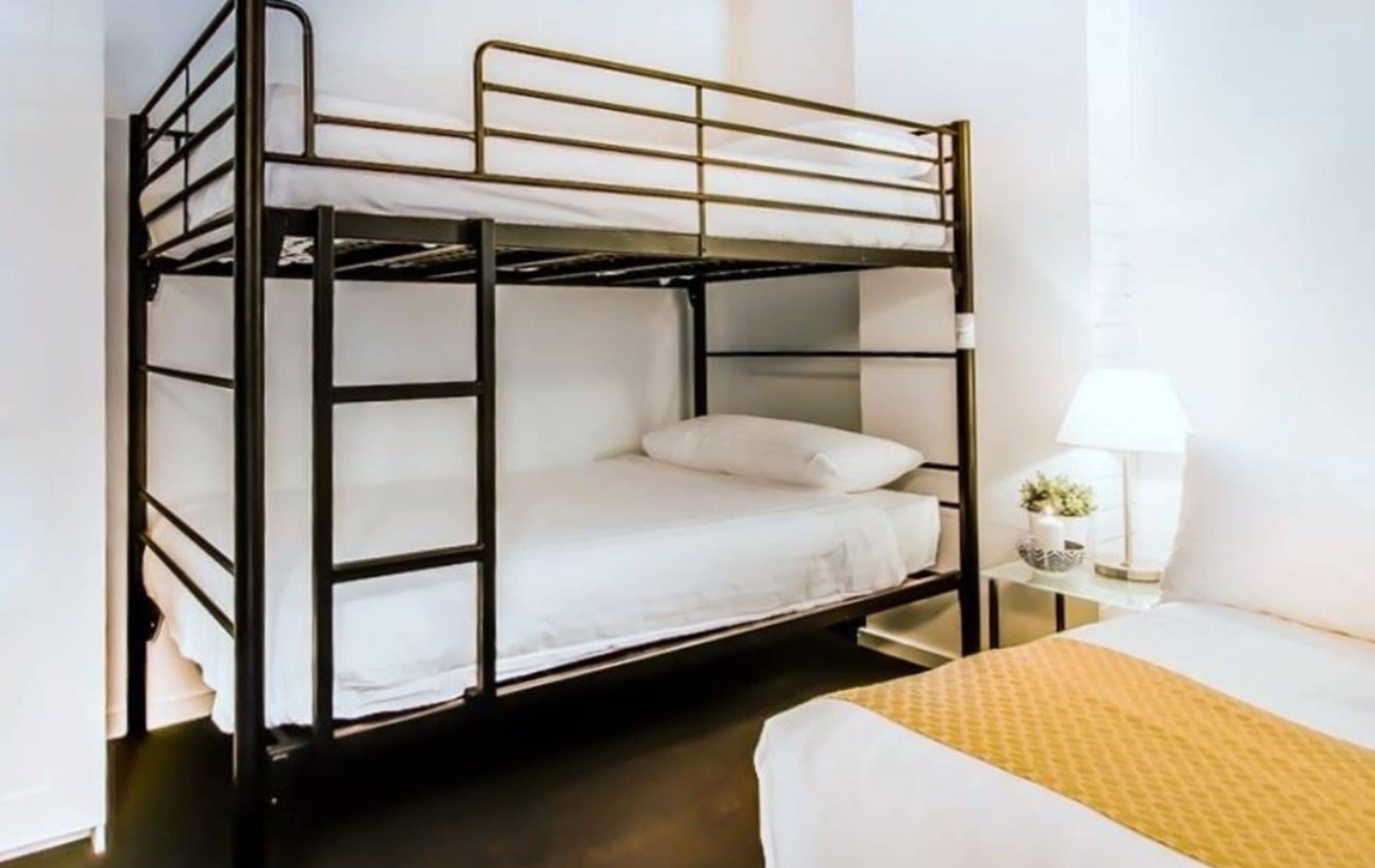 A bunk bed with white bedding and a small bedside table with a lamp and a plant.