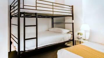 A bunk bed with white bedding and a small bedside table with a lamp and a plant.