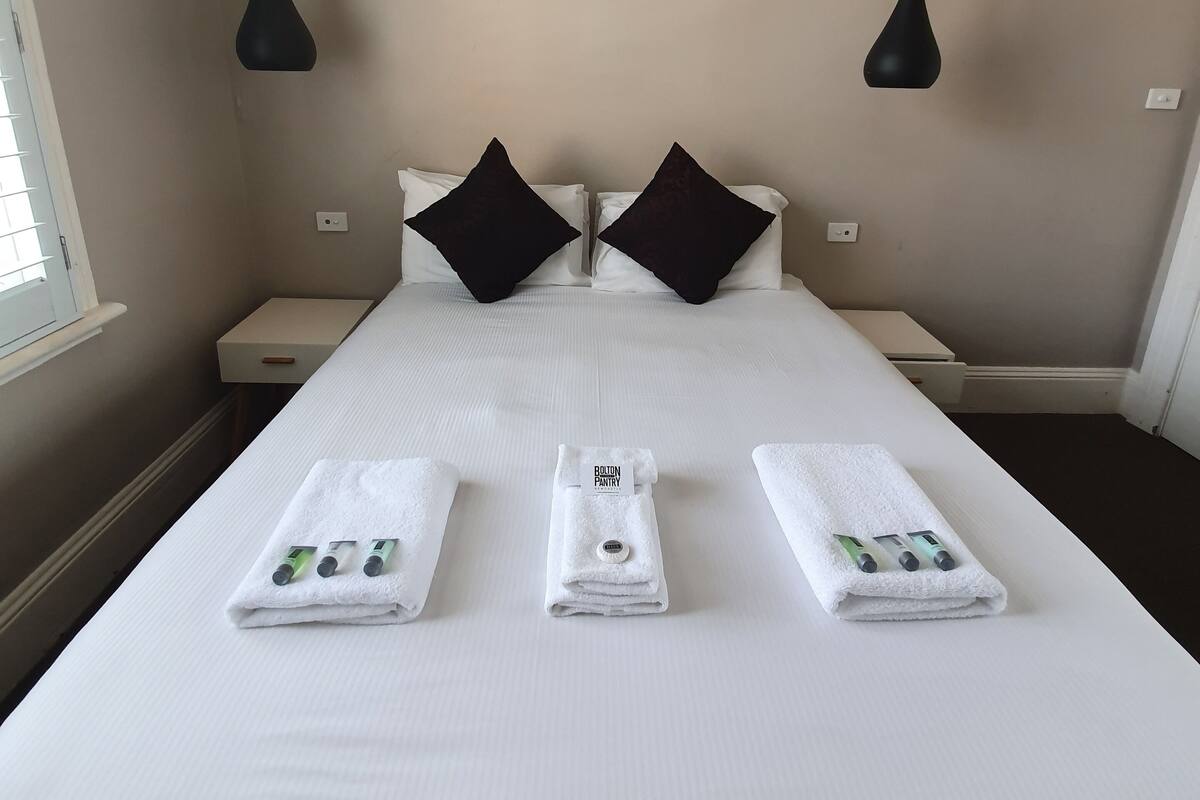 Una cama bien hecha con sábanas blancas, dos almohadas negras y dos lámparas colgantes negras.