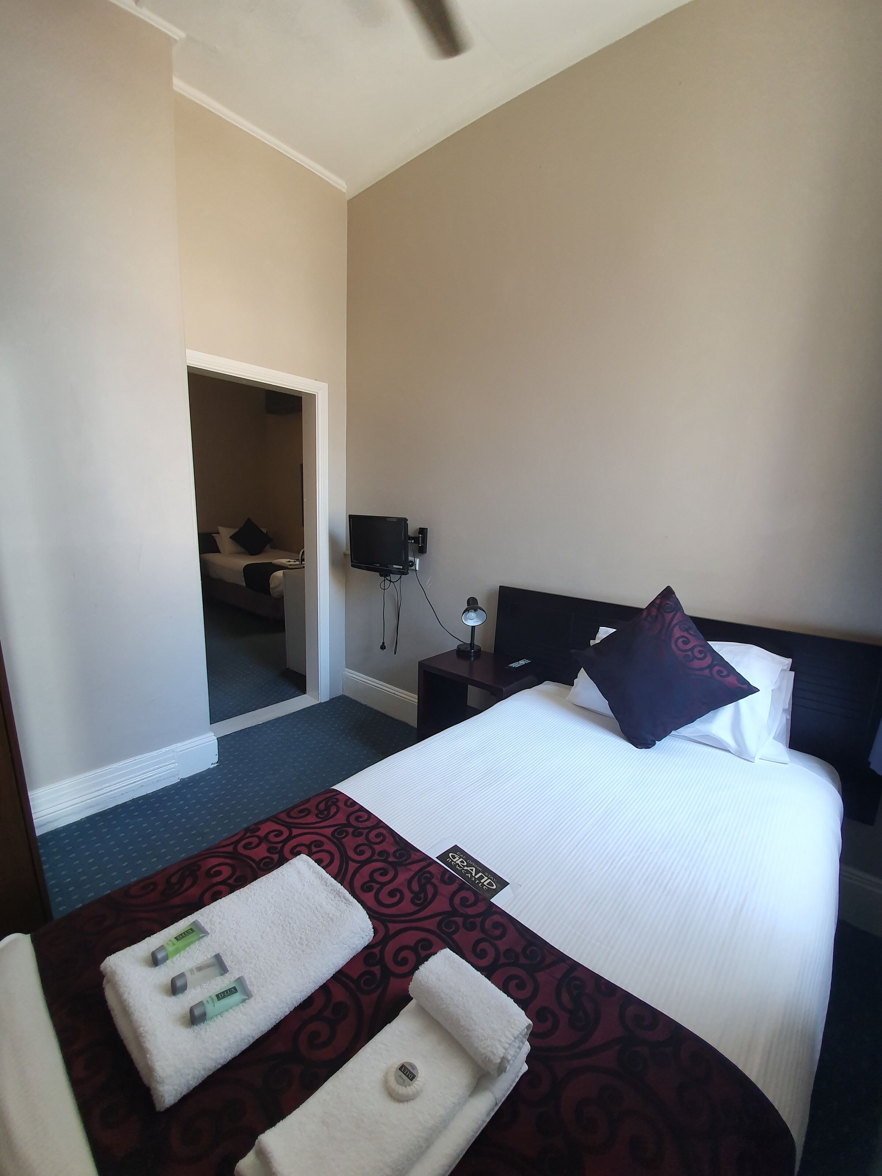 Ein Hotelzimmer mit einem Bett, einem Fernseher, einem Nachttisch und einem durch eine offene Tür einsehbaren Badezimmer.