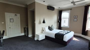 A hotel room with a bed, bedside tables, a desk, a ceiling fan, and a window with curtains.