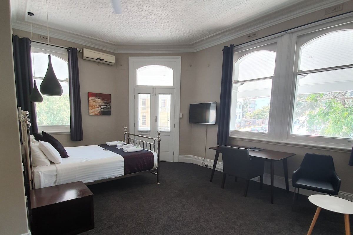 Habitación de hotel con cama, escritorio, silla y ventilador de techo.