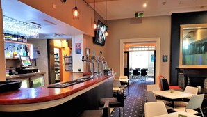 A bar area with a counter, multiple taps, and a digital screen. There are tables and chairs in the adjacent dining area. - The Grand Hotel Newcastle (Newcastle)