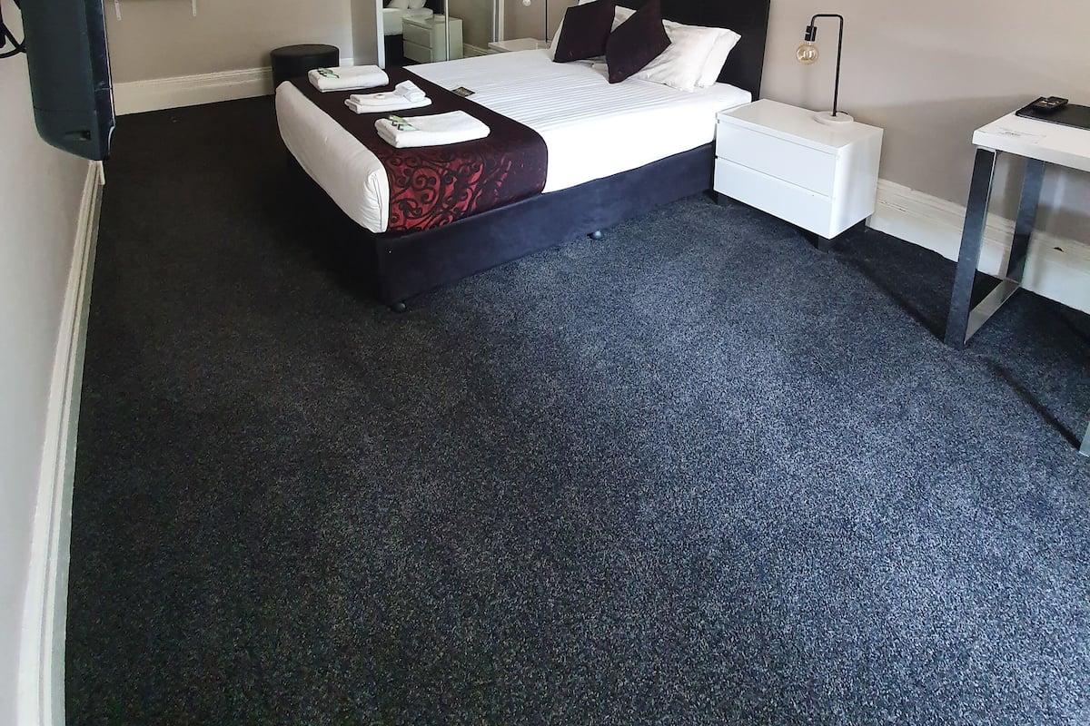 Habitación de hotel con una cama, una mesita de noche, un espejo, un ventilador de techo y un televisor de pared.