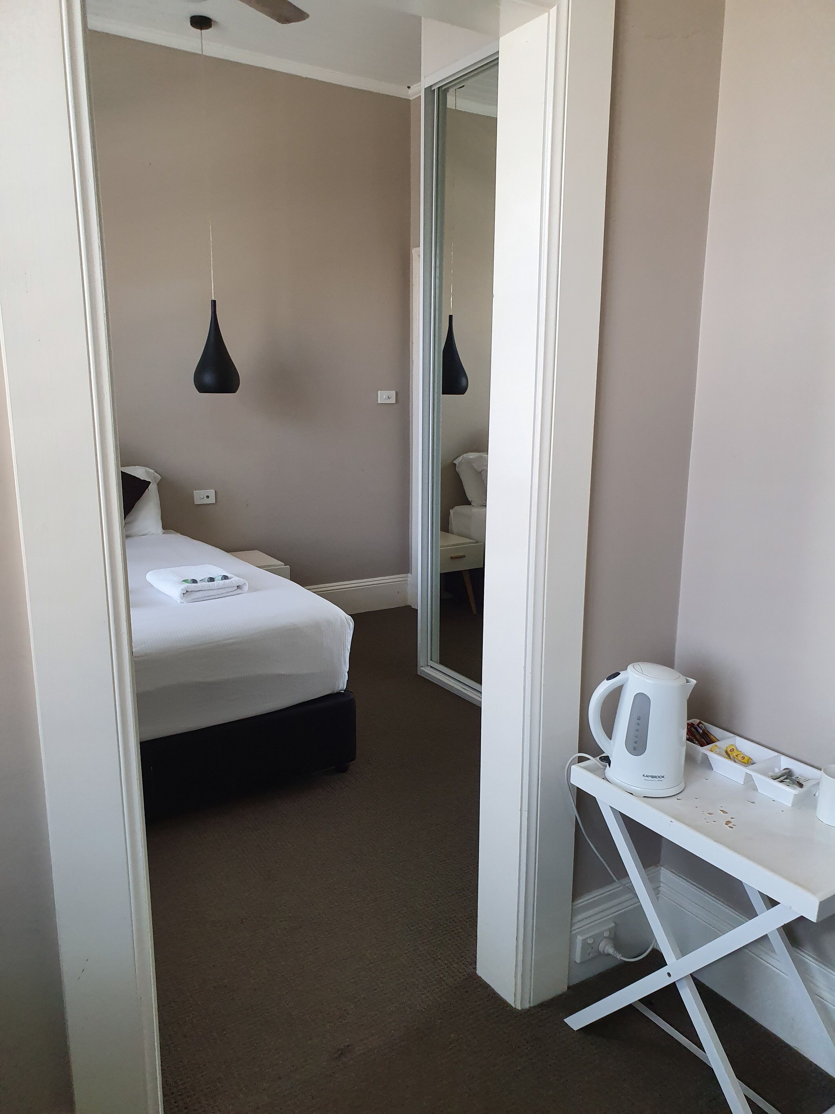 A hotel room with a bed, a white desk with a kettle, and a mirror.