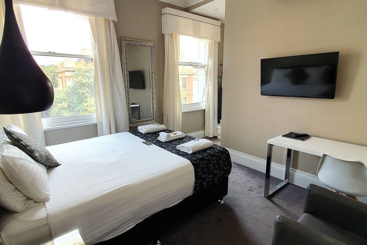 Una habitación de hotel con una cama grande, un escritorio, una silla, un televisor y una ventana con cortinas.