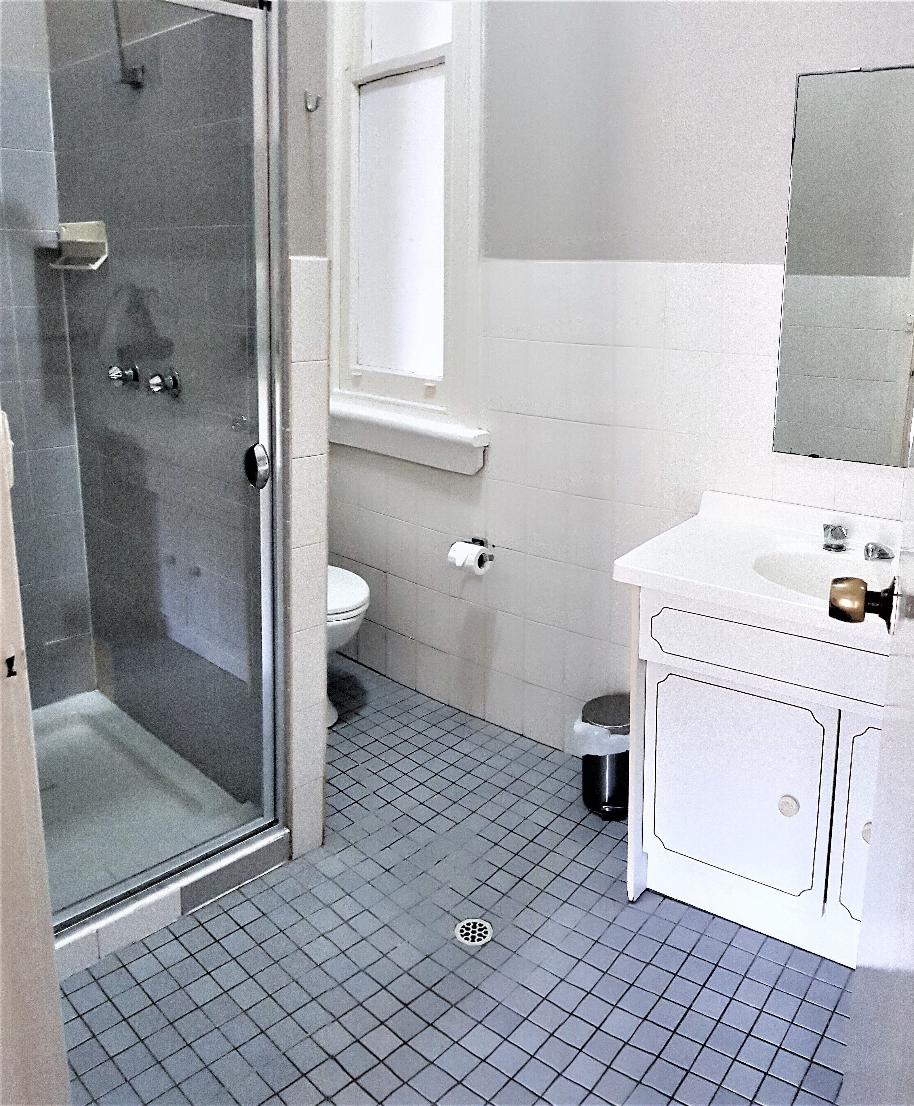 A bathroom with a glass shower enclosure, a toilet, a sink with a mirror, and a window above the toilet.