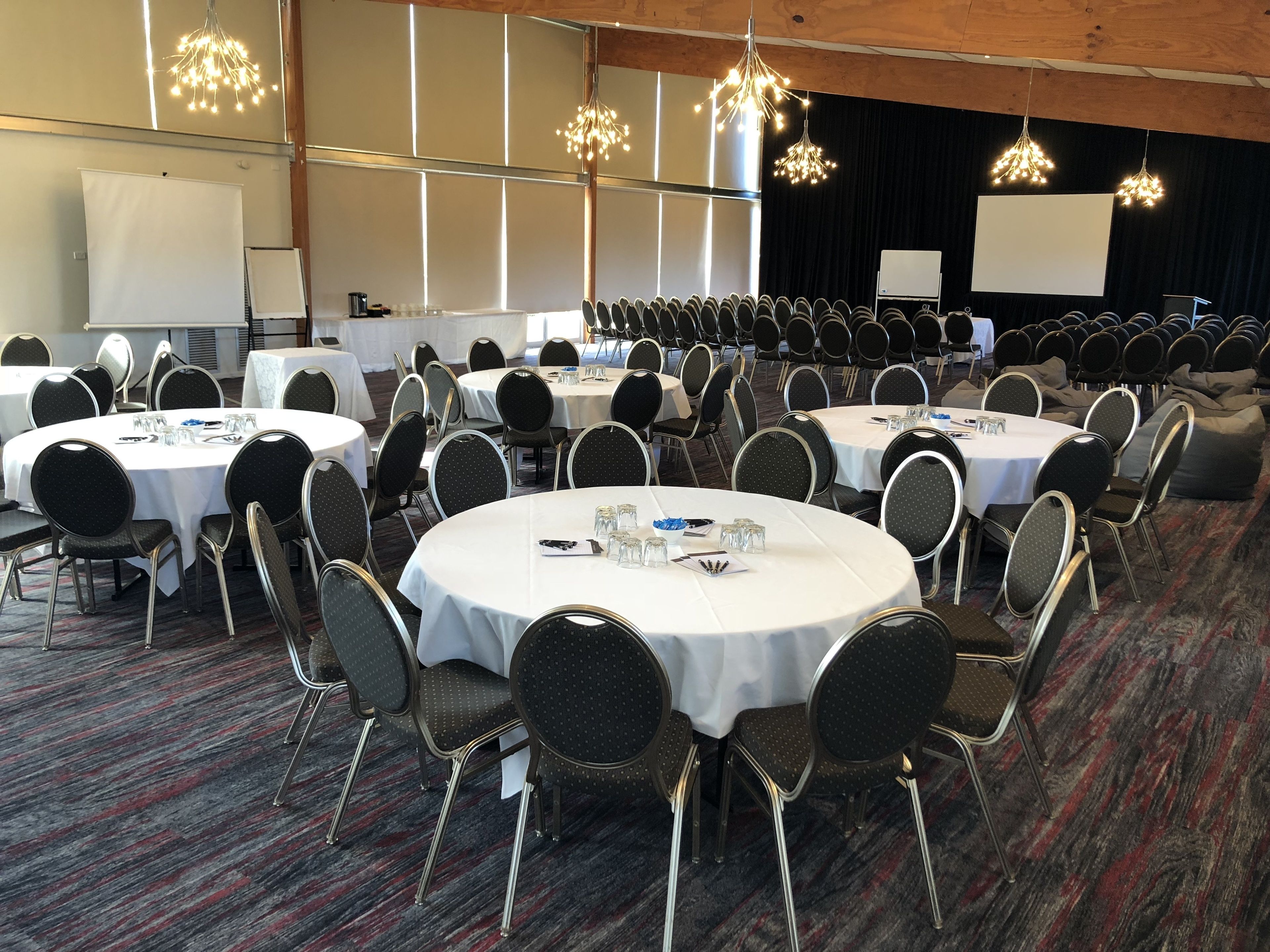 A conference room with round tables, black chairs, and white tablecloths.