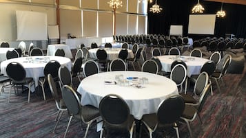 A conference room with round tables, black chairs, and white tablecloths.